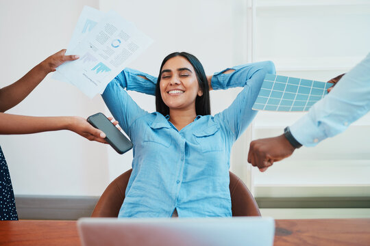 Young South Asian woman relaxes in office chair while coworkers make demands