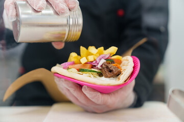 Chef seasoning pita souvlaki dish with salt. Cook preparing traditional Greek fast food in restaurant kitchen