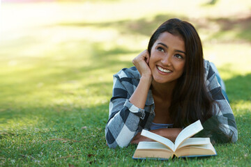 Relaxing with a good book. a young woman lying on grass and reading a book.