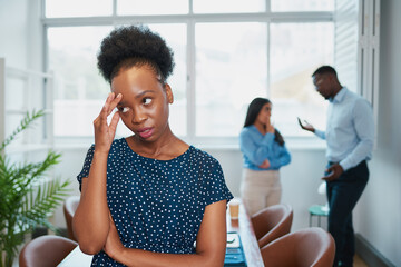 Young Black woman looks upset while colleagues talk behind her back office drama