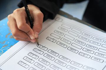 Close up photo of kid hand doing math test on paper in learning activity in classroom