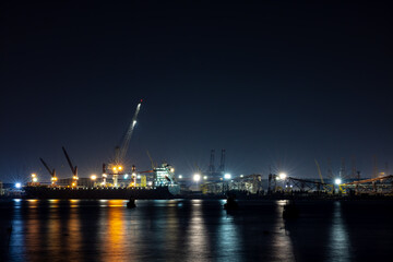 Fototapeta na wymiar shipyard dry dock maintenance and repair container ship transport and oil ship tanker, crane work and commercial port reflection in water, business and industry zone at night over lighting 