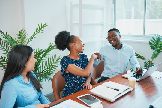 Two colleagues bump fists during office meeting in boardroom, celebrate win