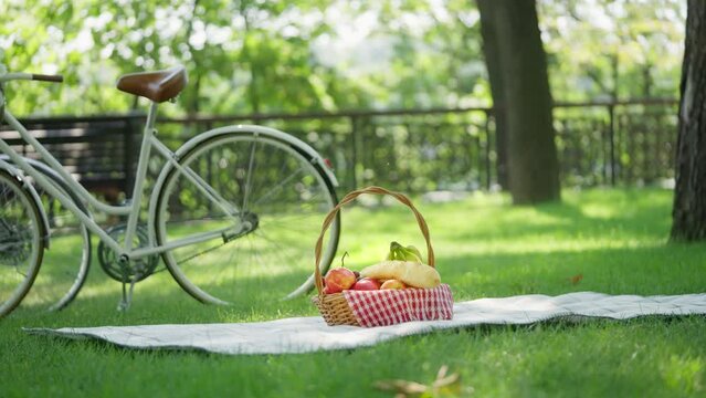 Picnic basket full of fresh fruit standing on blanket with city bikes nearby