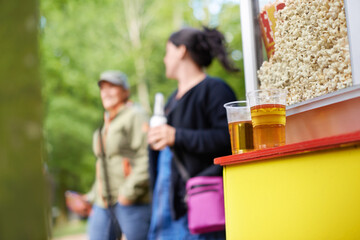 Heading to the kiosk. two beers resting on a popcorn machine with two women in the background.