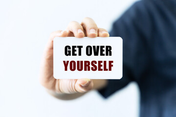 Get over yourself text on blank business card being held by a woman's hand with blurred background. Business concept about get over yourself.