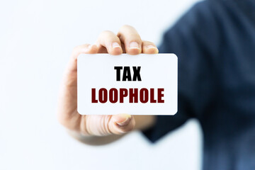Tax loophole text on blank business card being held by a woman's hand with blurred background. Business concept about tax loophole.