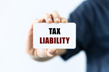 Tax liability text on blank business card being held by a woman's hand with blurred background. Business concept about tax liability.