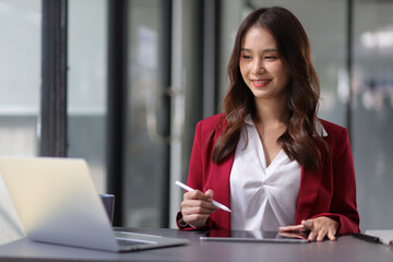 Young beautiful asian businesswoman in office working with laptop using tablet to work with electronic documents.