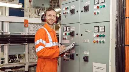 Young marine engineer making notes in engine room log book. Offshore professional safety checklist. 