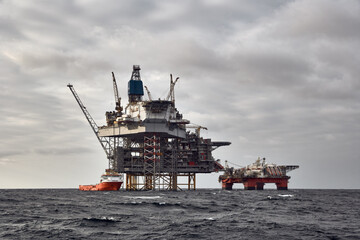 Offshore oil and gas platform with supply vessel doing cargo operations.  Dark sky in the North Sea.