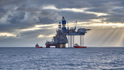 Beautiful view of a jack up drilling rig and supply vessels in the sea at sunset.