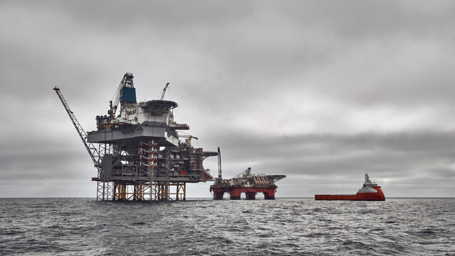 Panorama of Jack up drilling rig, semi submersible platform and supply vessel on a dark cloudy day in the sea. North Sea oil and gas. 