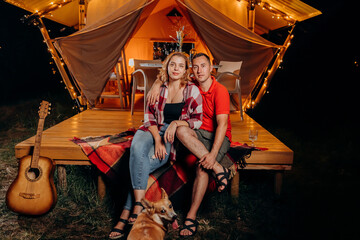 Happy lovely couple relaxing in glamping on evening near cozy bonfire. Luxury camping tent for outdoor recreation and recreation. Lifestyle concept