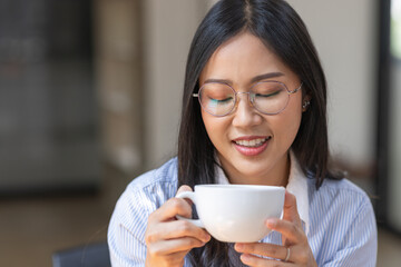 Beautiful young Asian woman working on laptop computer while sitting at the plan office space after working hours, Asian woman drinking coffee