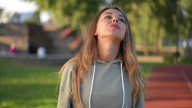 Portrait of confident woman stretching neck muscles warming up outdoors. Young beautiful Caucasian sportswoman exercising in park at sunset. Sport and lifestyle concept
