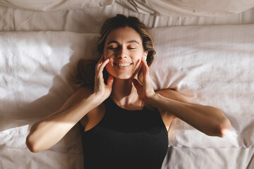 Naklejka premium Beautiful young woman listening music in wireless headphones at home lying on bed. Young pretty woman person are happy and enjoy with music by using earphone for listen a sound audio in bedroom.
