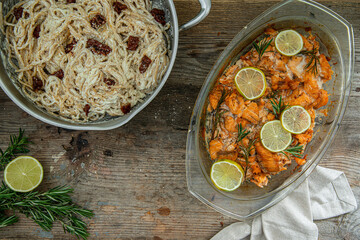 Salmon bites baked in oven with lime and rosemary, and pasta in pan on rustic wooden table.