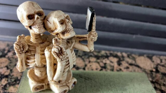 Skeletons without legs take a selfie look at a mobile phone they smile with all their teeth and show two fingers up as if Victor comic sculpture Two funny skeletons