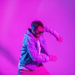Stylish handsome young hip hop dancer man in trendy fashion denim clothes dancing in studio with creative pink and blue neon light