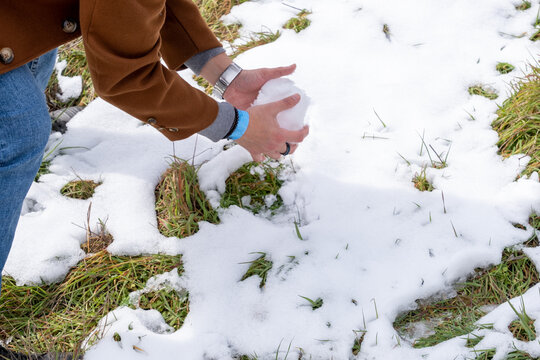 Hombre joven de raza caucásica haciendo una bola de nieve en un parque de Burgos con la hierba nevada de fondo. - Powered by Adobe