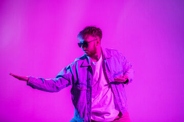 Handsome stylish dancer guy with sunglasses in fashion denim clothes with a jacket. dancing in a creative studio with pink and blue light