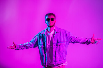 Fashion hip hop dancer handsome guy in stylish casual denim clothes with black sunglasses dancing in the studio with creative pink and blue light