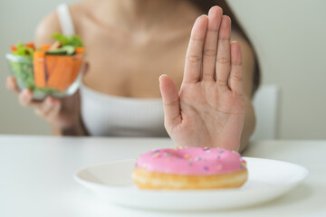 Diet, Dieting asian young woman, girl hand push out, deny sweet donut on plate, dish and choose to eat green salad vegetables in bowl on table, food good healthy, health person, female weight loss.