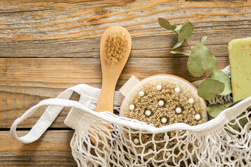 Spa composition with massage brushes and hygiene items in a mesh shopping bag on a wooden background, , top view, eco concept.