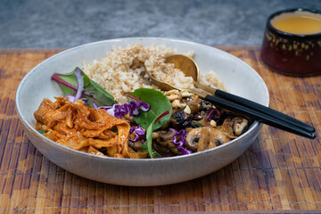 Asian vegan bowl consisting of  brown rice,  stir fried mushrooms, curd skin