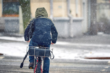 Man delivering pizza on bicycle during snow strom. Courier cycling on snowy street. Delivery food...