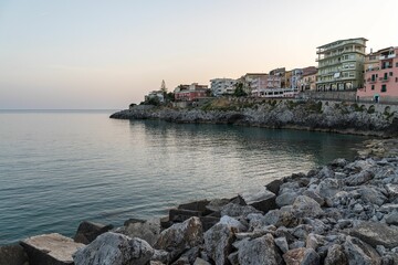 Image of a shore with stones and buildings on the left during sunset in Marina di Camerota, Campania