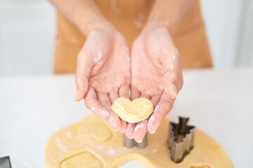 Obraz na płótnie Canvas Love And Care Concept. Closeup above top view of unrecognizable asian woman baking cake in the kitchen and holding dough in heart shape in hands, housewife cooking .