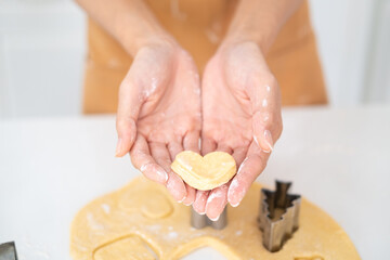 Love And Care Concept. Closeup above top view of unrecognizable asian woman baking cake in the kitchen and holding dough in heart shape in hands, housewife cooking .
