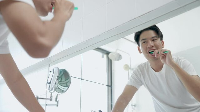 Happy Asian man brushing her teeth with a toothbrush in the bathroom in bright morning.