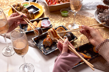 Portrait of three beautiful young women eating japanese food and drinking wine at home.