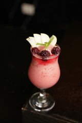 Vertical closeup shot of a glass with a gourmet fruit smoothie with sliced apples and blackberries