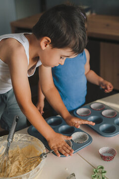 Caucasian little boy and her beautiful baby siste pouring raw dough into mold for baking cookies, muffins in kitchen at home. Homemade cooking, healthy food