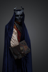 Shot of dark cultist dressed in horned mask and robe holding book.