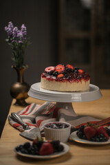 Delicious cake with fresh berries on a white ceramic stand on a wooden table