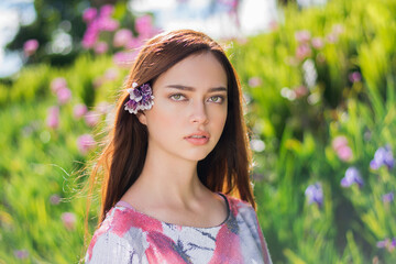 Young beautiful brunette female with a flower in her hair posing on a floral field