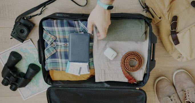 Close-up of male hand packing suitcase putting plane ticket and passport in bag preparing luggage for travelling. Baggage and tourism concept.