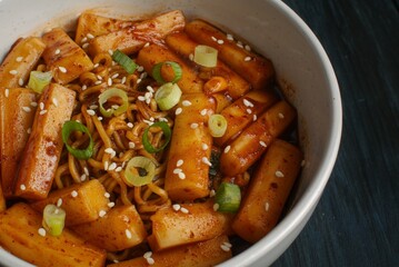 Rapokki or rabokki stand for ramyeon and teokpokki, a korean rice cake mix with instan noodles garnish with sesame seed and cut chives. Isolated in dark blue background