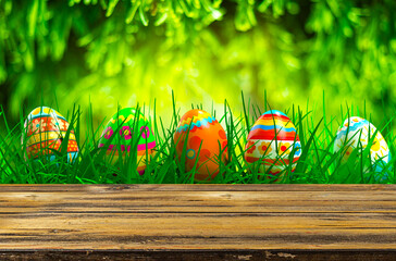 Empty wooden table with easter egg and blurred green nature background. Abstract blurry Easter scene with bokeh and warm sunlight. Concept banner for products display