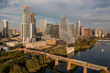 Fototapeta premium Downtown, Austin Texas skyline and cityscape with passing train along bridge over Lady Bird Lake during golden hour sunset