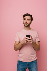 Displeased man using mobile phone and looking away isolated over pink wall
