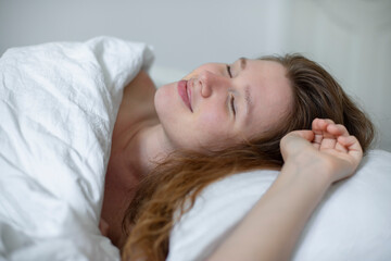 Fototapeta na wymiar Young happy beautiful sleepy woman in the bed in bedroom at home in the morning lying under white blanket, enjoy resting, sleep well, wake up and smile. Good morning