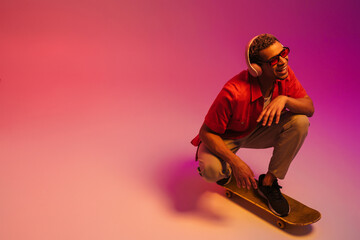 Cheerful african guy riding on skateboard isolated over multicolored neon background