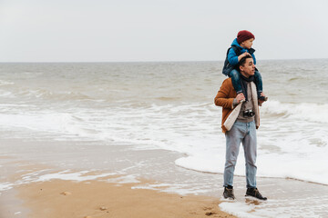 Father carrying on shoulders his son while walking together on beach