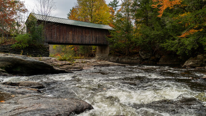 Covered bridge over river and surrounded by fall foliage in Vermont autumn landscape.